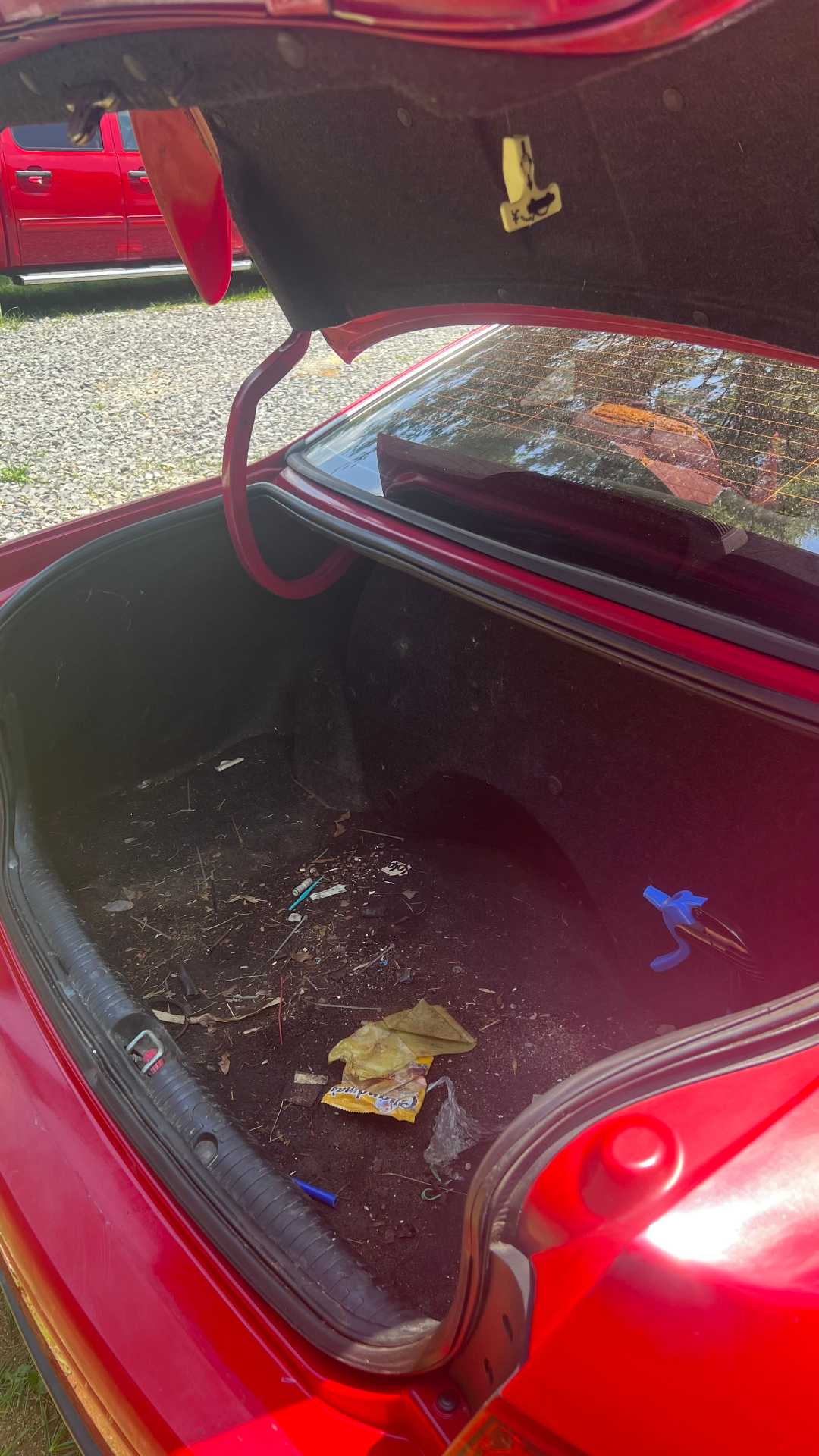 Dirty sedan trunk before detailing — debris, leaves, and food wrappers on the trunk floor